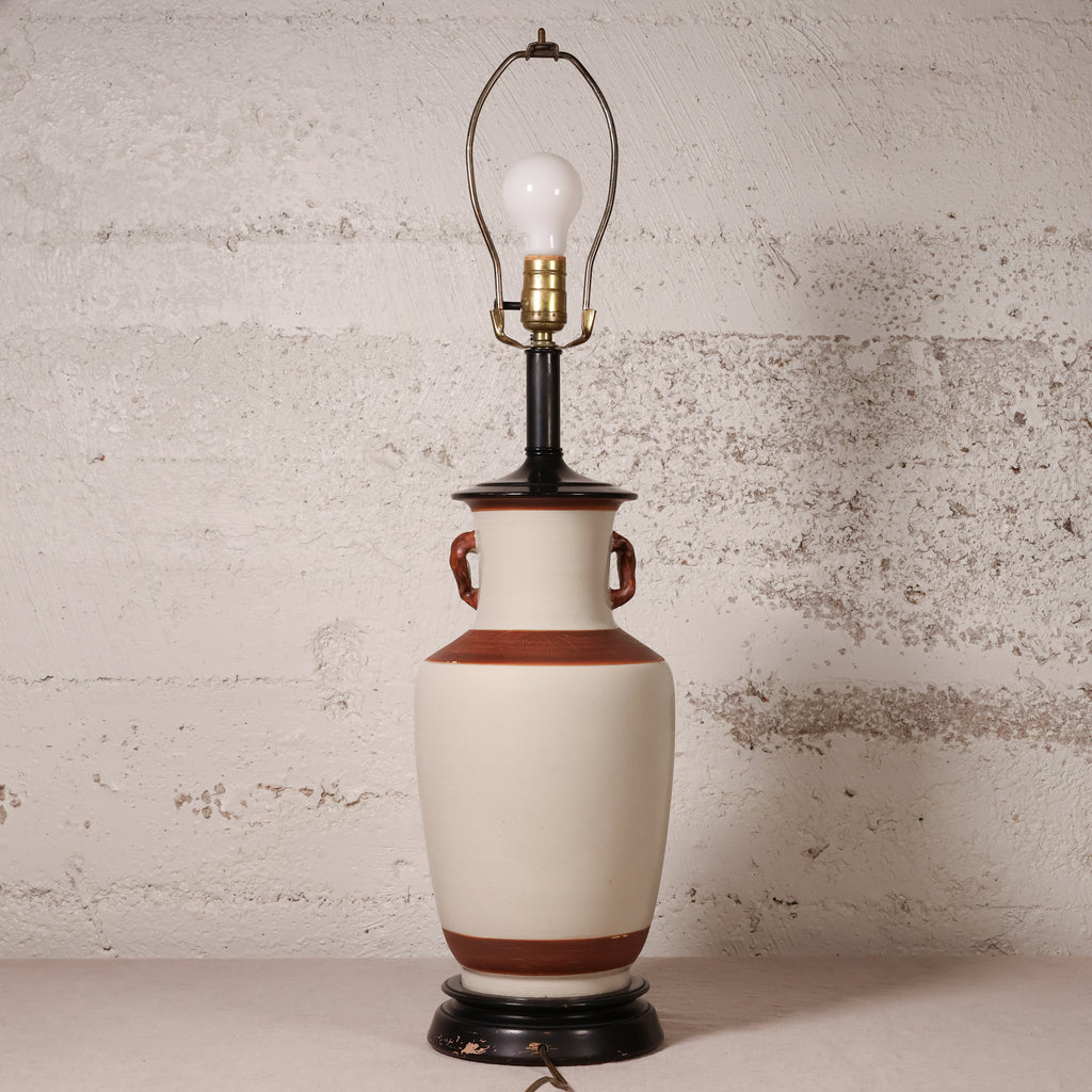 A vintage-style ceramic table lamp with a cream-colored body, brown bands, and a black base, featuring a wire shade and a visible light bulb.