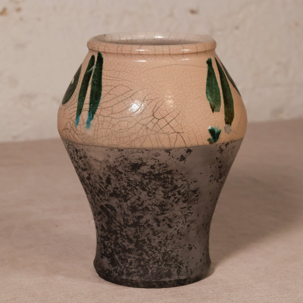 A handmade ceramic vase with a textured, crackled finish. The upper half features a warm beige glaze with green leaf-like patterns and blue accents, while the lower half has a dark, distressed charcoal gray finish.