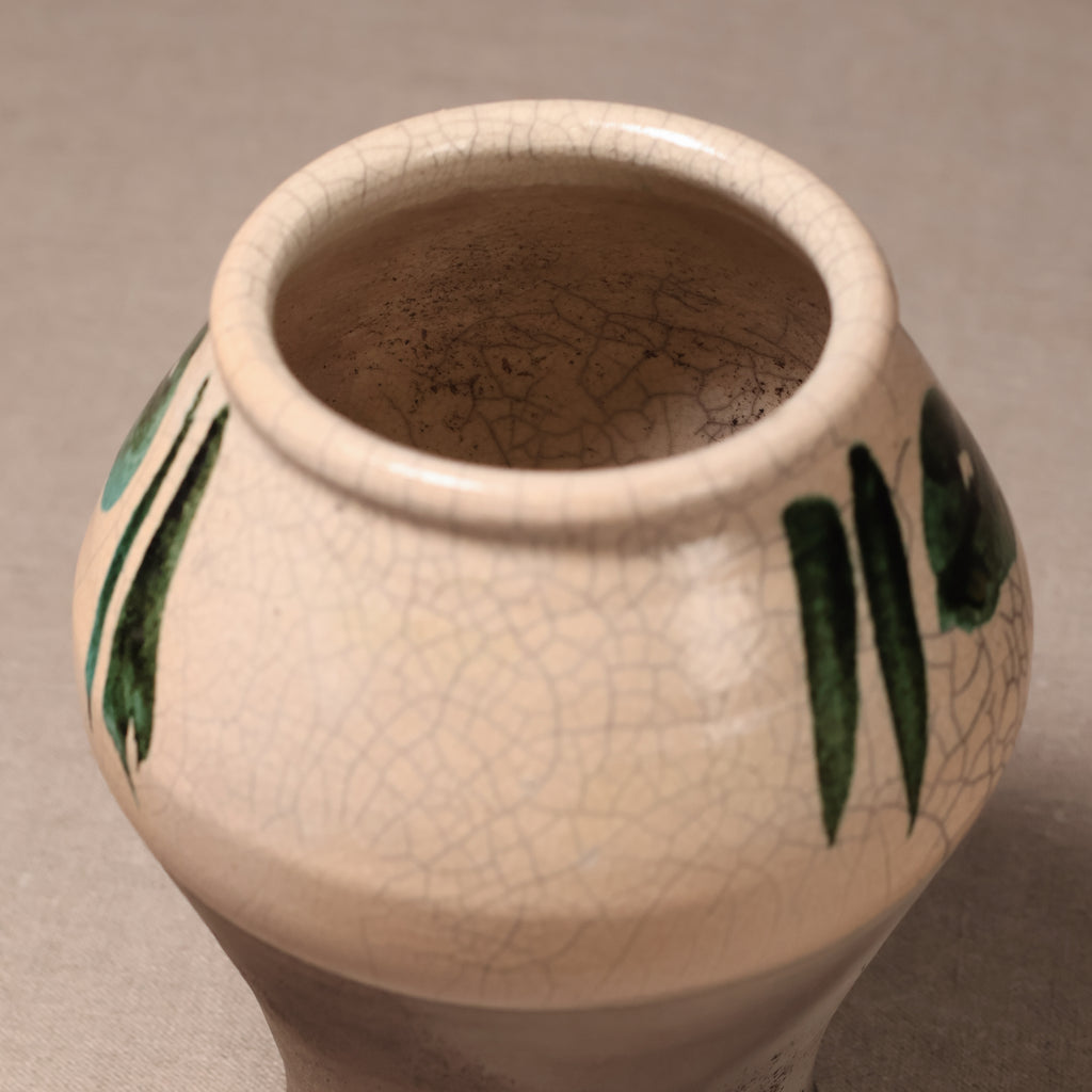 A ceramic vase with a cream-colored glaze featuring a crackle pattern and hand-painted green leaf motifs, shown from a top-down angle on a neutral gray background.
