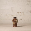 Small brown ceramic vase with floral patterns on a textured beige background