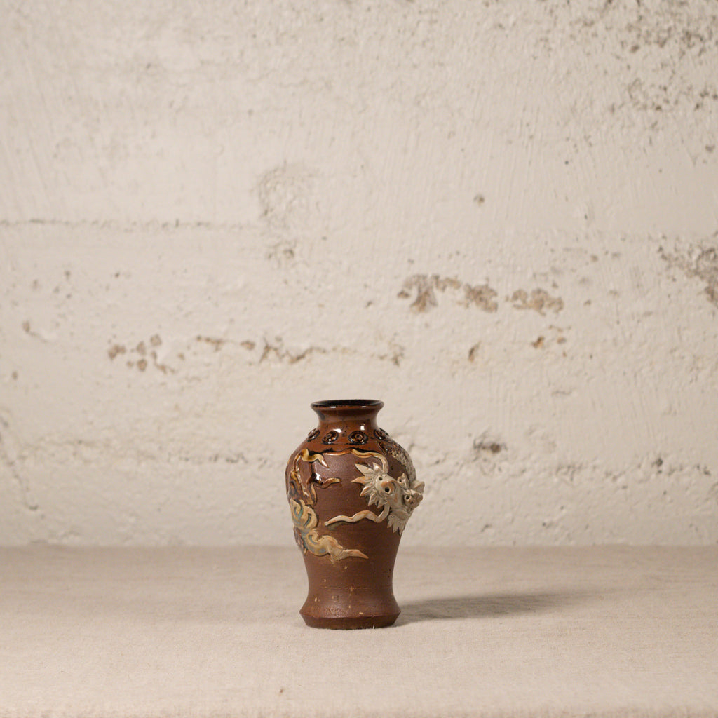 Small brown ceramic vase with floral patterns on a textured beige background