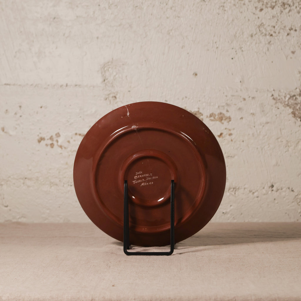 Brown ceramic plate on a stand against a textured beige wall