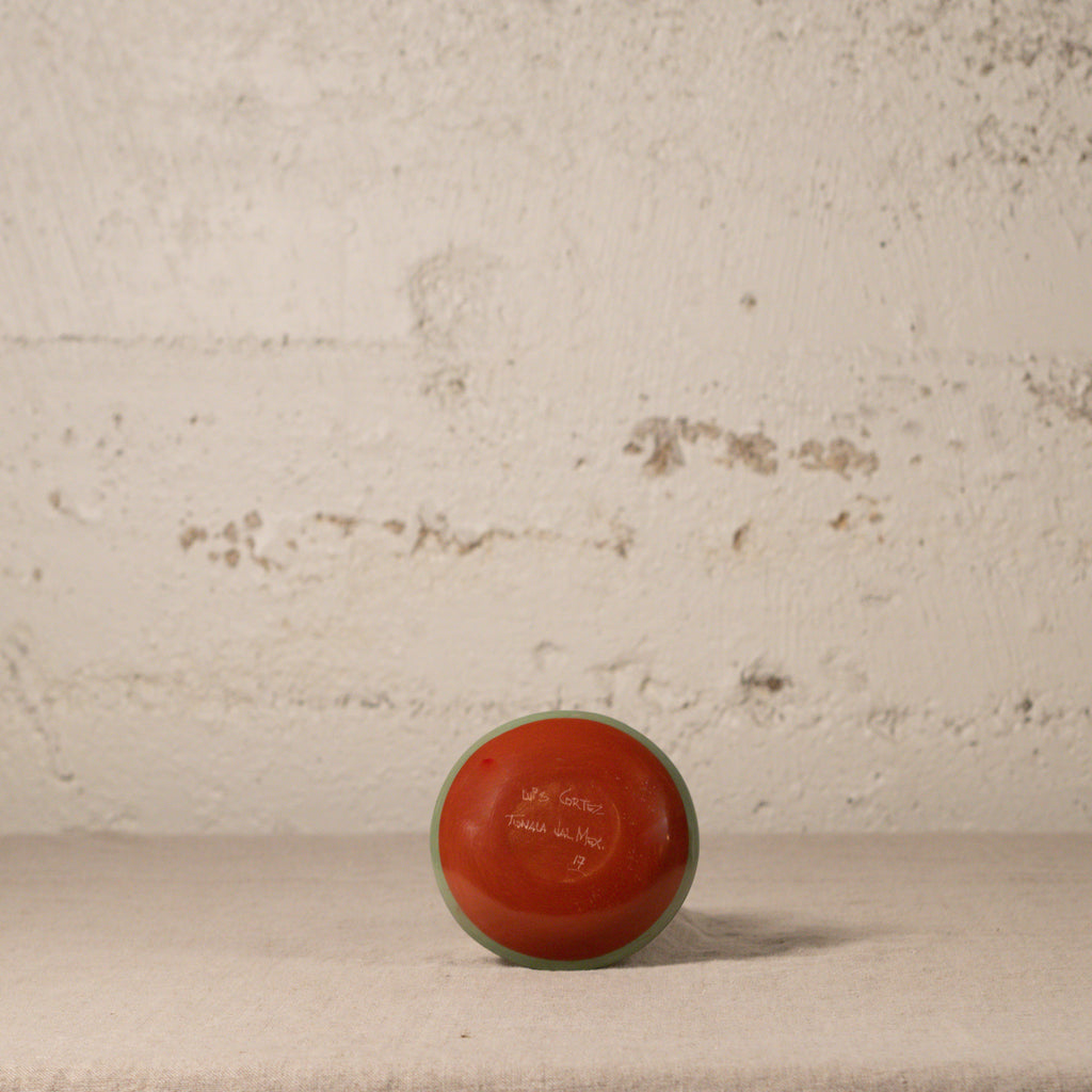 Red ceramic vase on a textured surface with a neutral background