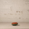 Small round object with red top and green base on a textured surface with a beige wall background