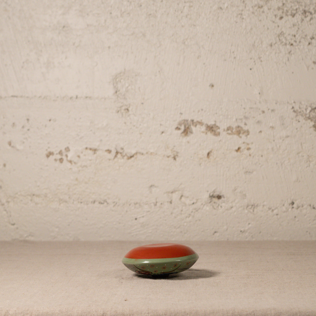 Small round object with red top and green base on a textured surface with a beige wall background