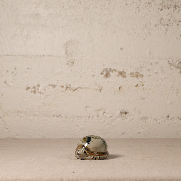 Small ceramic turtle on a textured beige surface with a neutral background