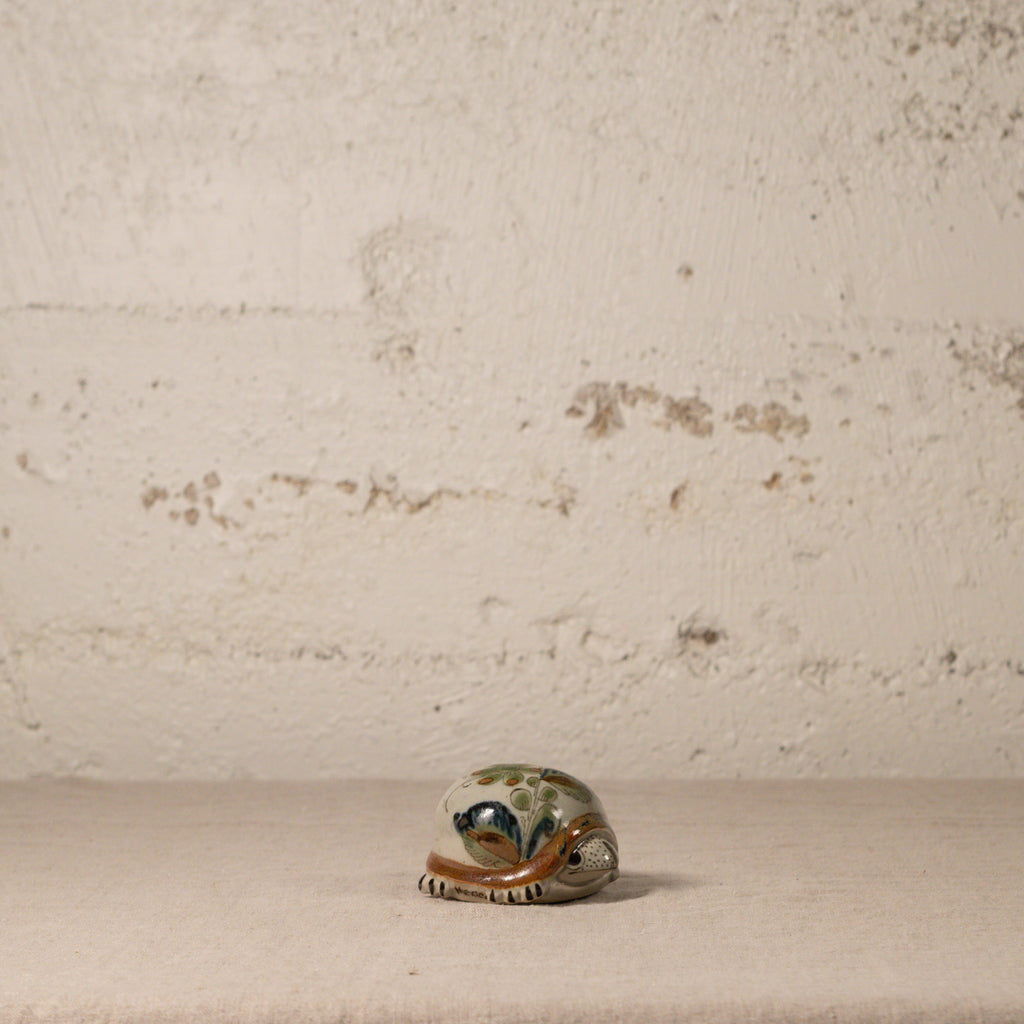 Small ceramic turtle figurine on a textured surface with a neutral background