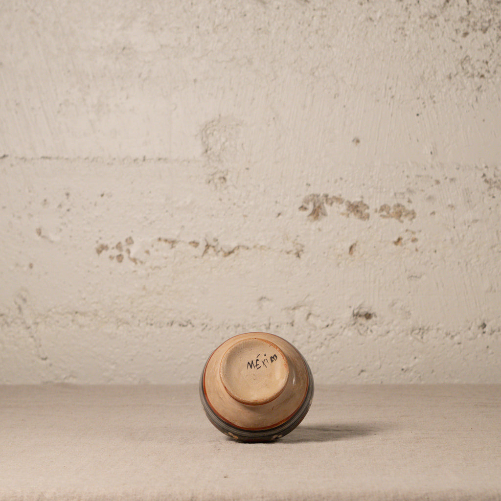 Small ceramic cup with 'MEXICO' written on it against a textured beige wall.