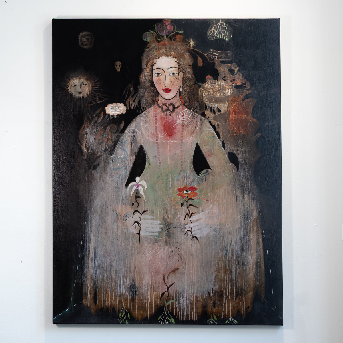 A vertical canvas painting hanging on a white wall, depicting a stylized woman in a pale dress against a dark background with surreal floral and celestial details.