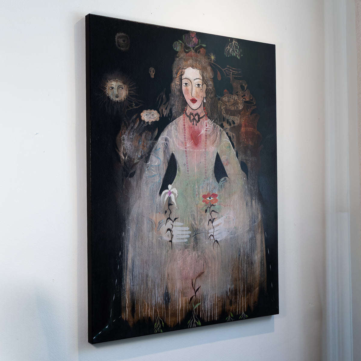 A vertical canvas wall art print featuring a surreal painted portrait of a woman in a pale dress holding flowers, displayed against a plain white wall.