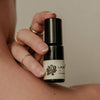 Hand holding a small black bottle with a white label against a neutral background