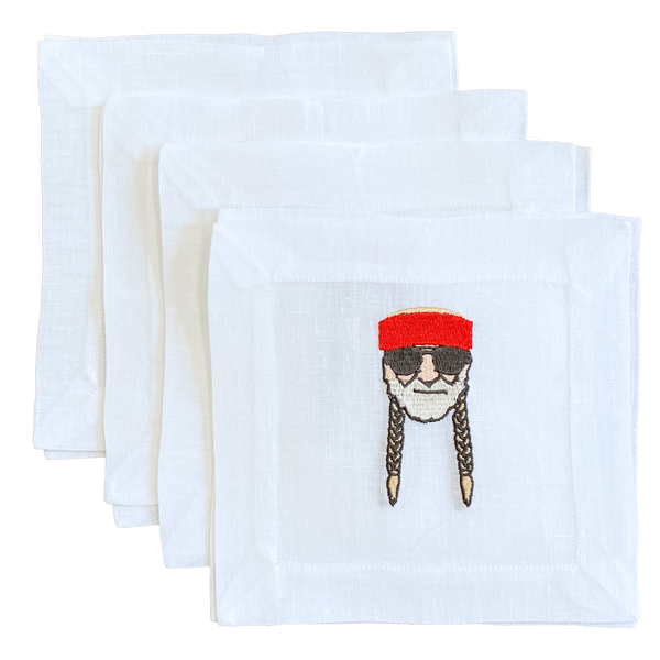 Four white square napkins stacked in a fan arrangement, with a small embroidered cartoon face wearing a red hat and sunglasses on the front napkin.
