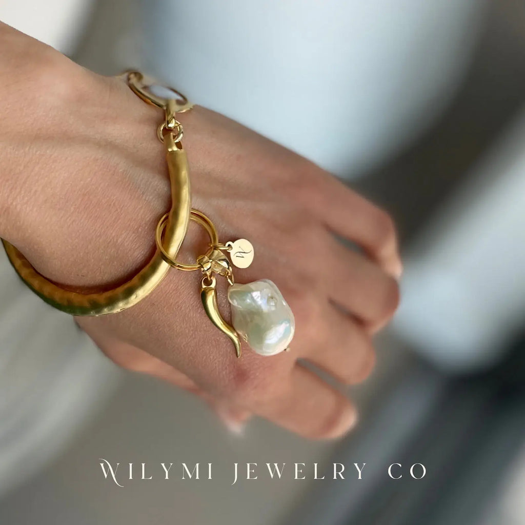 Gold bracelet with a pearl charm on a blurred background, featuring WILYMI JEWELRY CO branding.