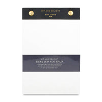 A Wit and Delight Desktop Notepad with cream-colored sheets, a dark charcoal gray top header, a matching dark gray middle band, and two gold metal grommets at the top.