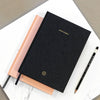 Black and pink notebooks with pencils on a marble surface