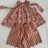 A children's two-piece outfit laid flat on a white fabric background, featuring a sleeveless top with a pink floral print on a beige base and matching striped tie straps, paired with striped shorts. A yellow tag reading 'JUMPMAN' is attached at the top.